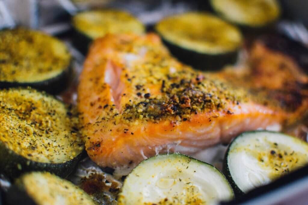 salmon filet topped with spices bakes alongside vegetables
