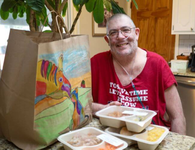DJ sitting in his kitchen with a Project Angel Heart meal bag and meals