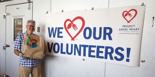 Jim Smith holding meal bag in front of we love our volunteers banner