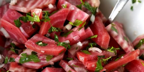 red and white sliced beets sprinkled with fresh green herbs in a white dish and silver-handled serving utensile